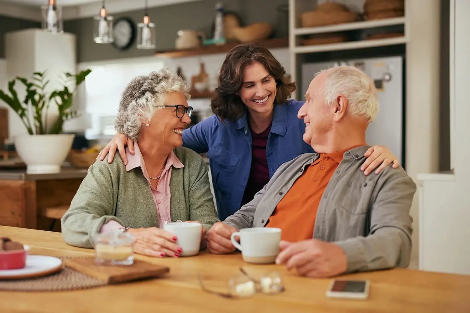 Adult woman sitting with aging parents at table having coffee Adult woman sitting with aging parents at table having coffee